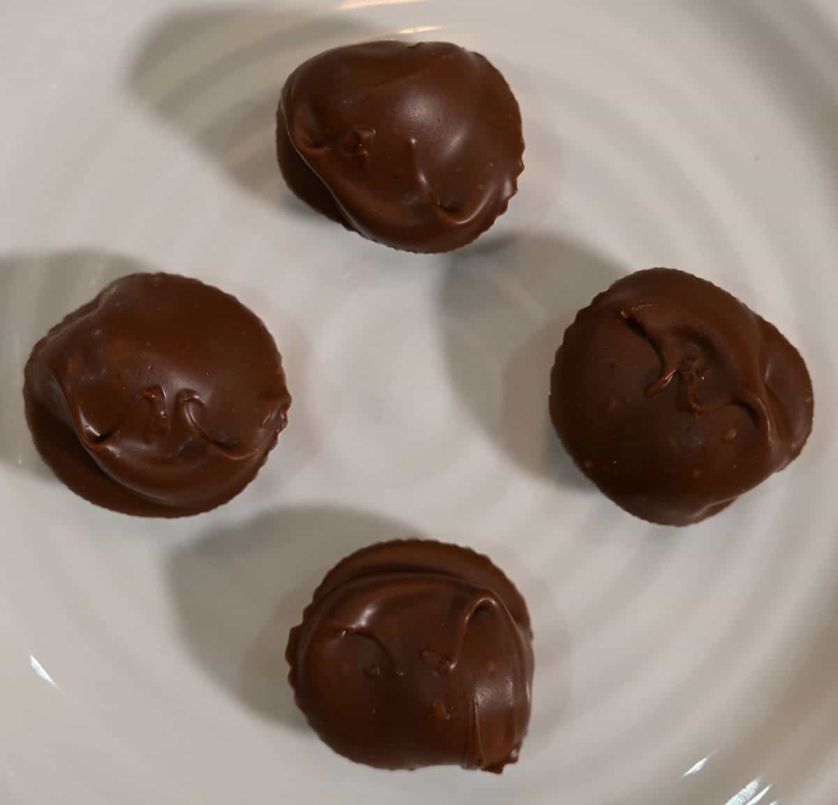 Closeup image of four chocolate covered macadamia nut chocolates on a white plate out of their wrapper.