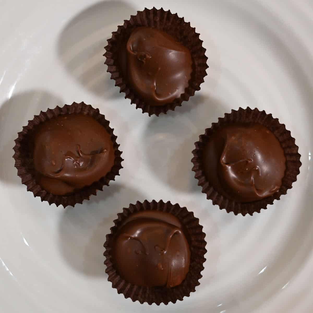 Closeup image of four chocolate covered macadamia nut chocolates in their wrapper on a plate.