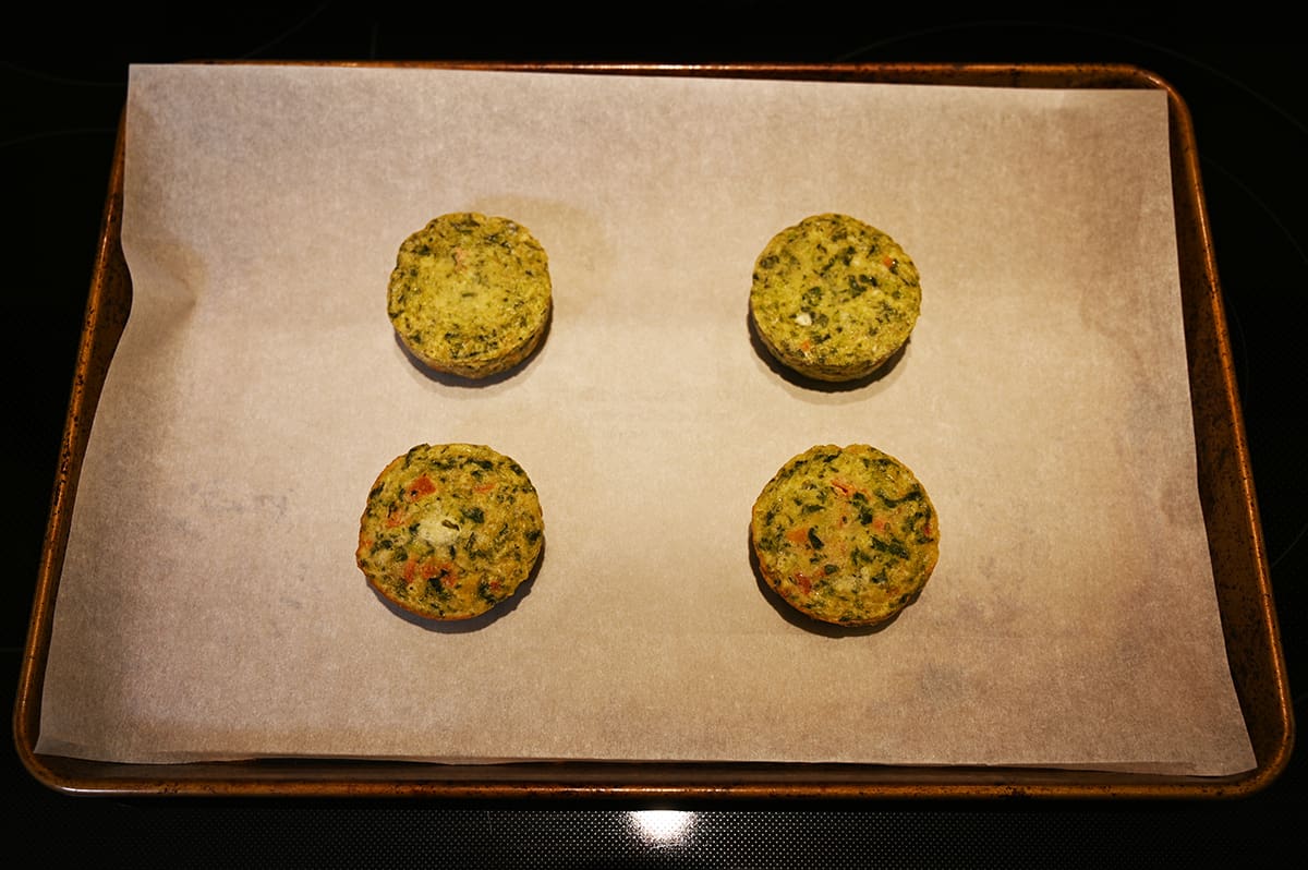 Image of a baking sheet in the oven with four spinach egg white frittatas on it cooking.