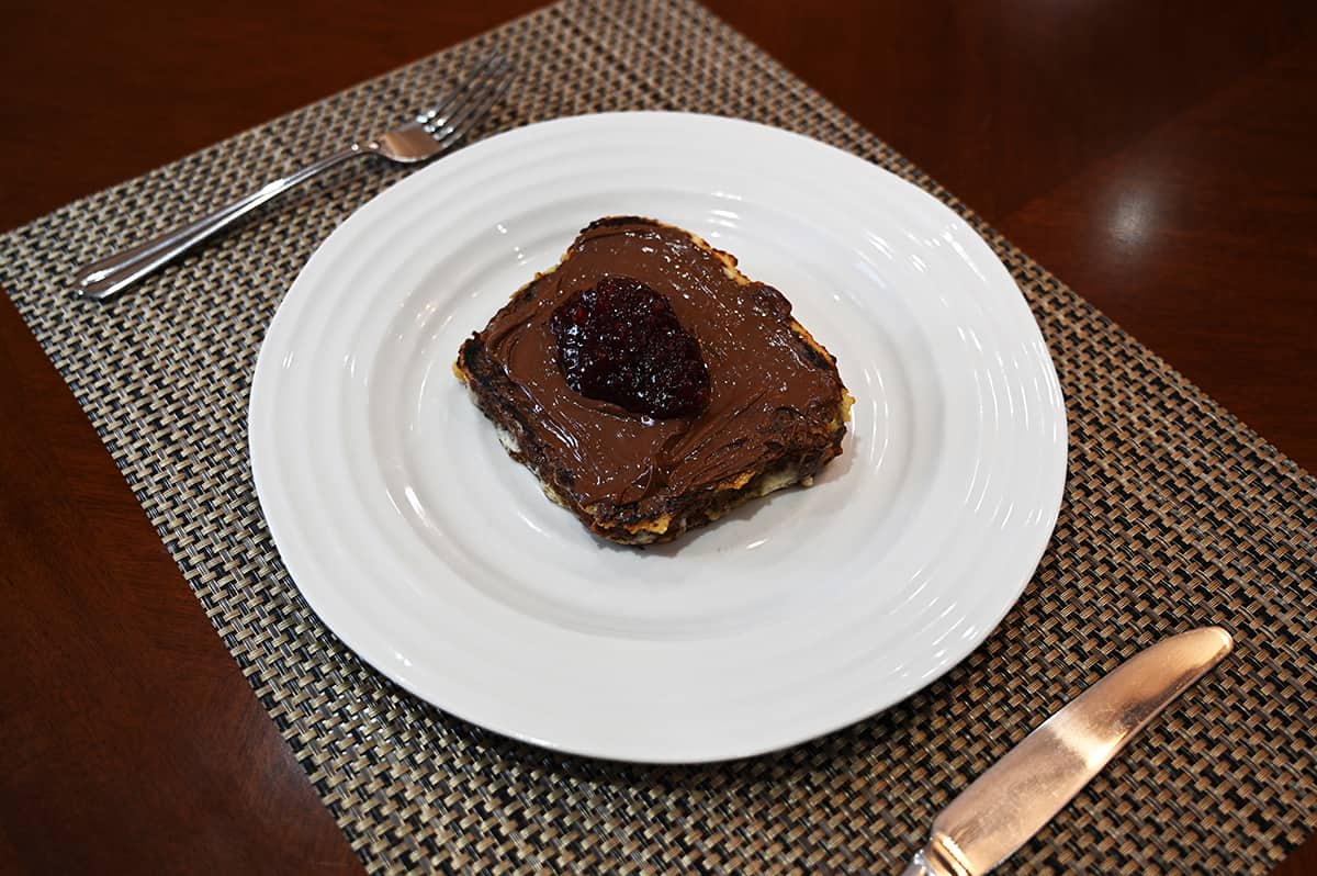 Side view image of banana bread french toast made out of the banana pecan loaf with jam and nutella on top and served on a white plate.