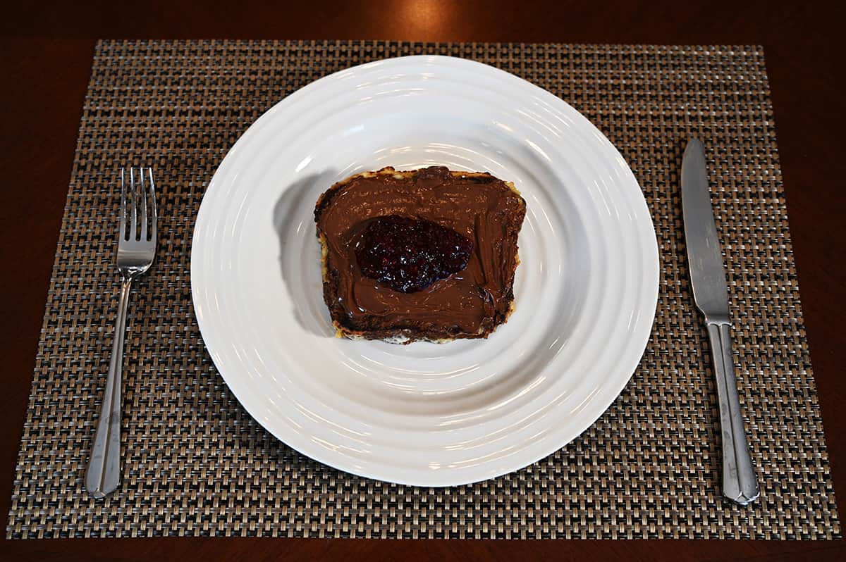 Top down image of banana bread french toast made out of the banana pecan loaf with jam and nutella on top and served on a white plate.