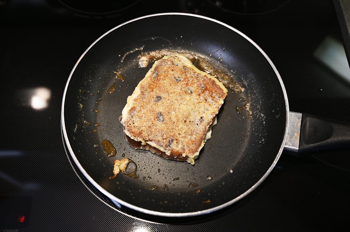 Image of one piece of banana bread french toast cooking in a frying pan.