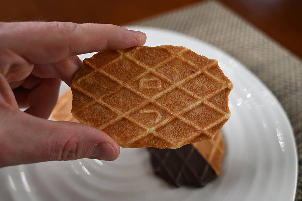 Image of a hand holding one original butter biscuit close to the camera with a plate of cookies in the background.