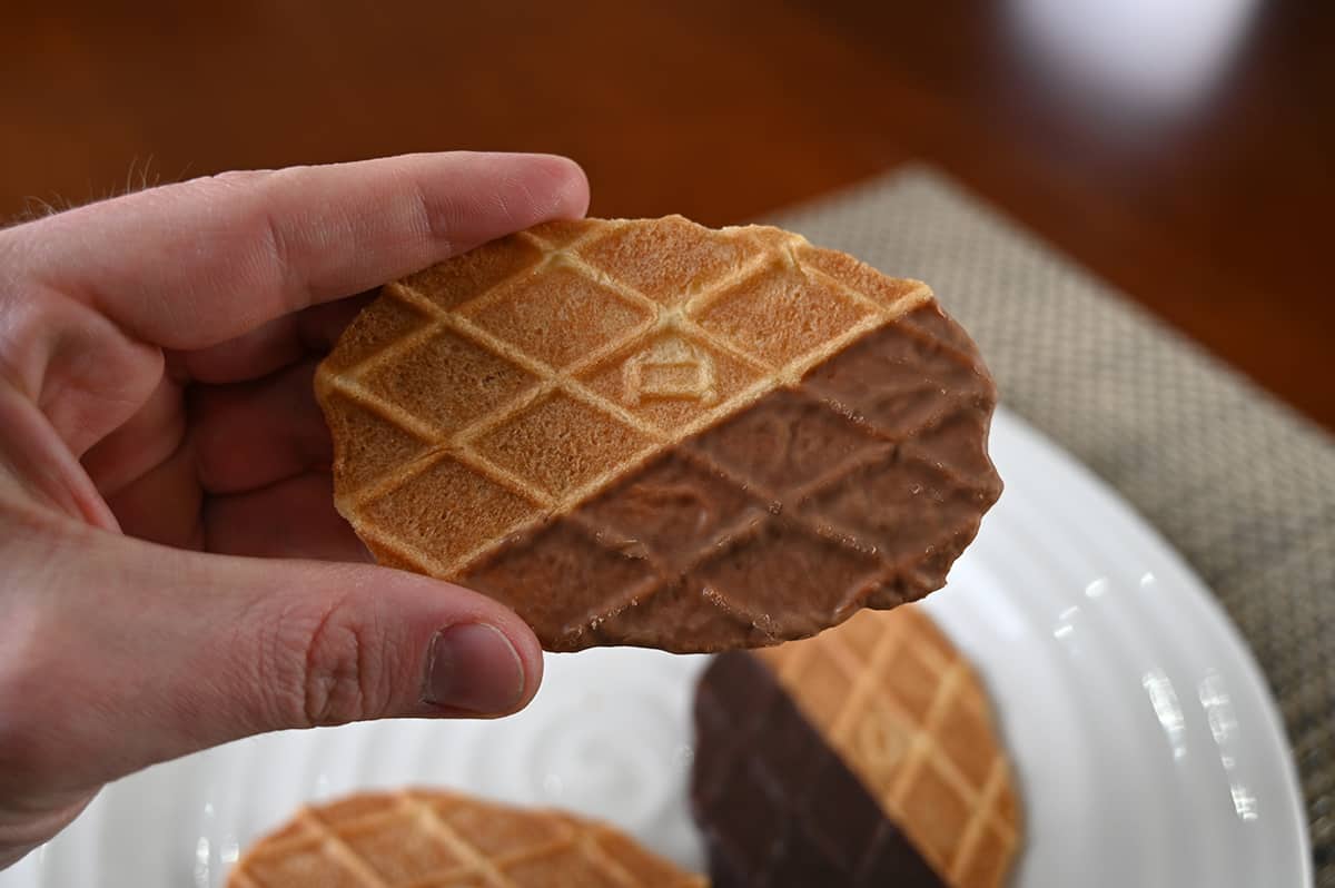 Closeup image of a hand holding one caramel-dipped biscuit close to the camera.