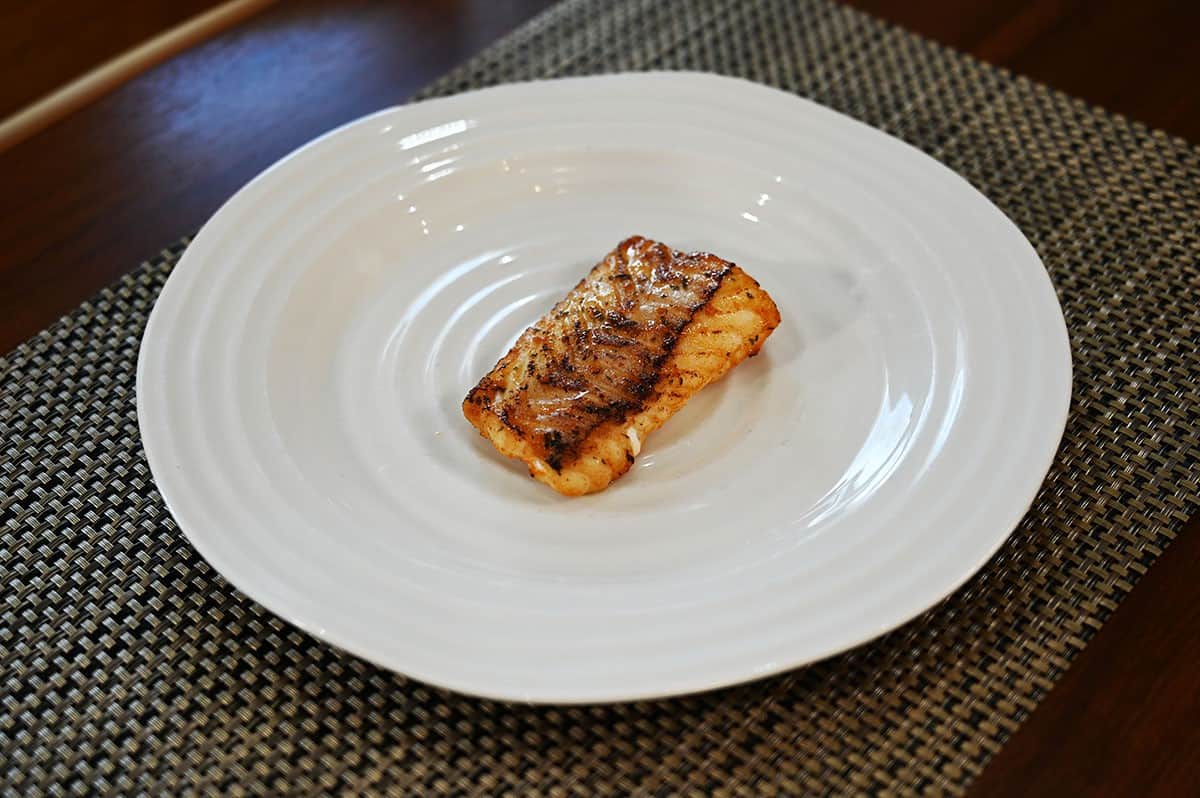 One fillet of cod cooked and served on a white plate. 