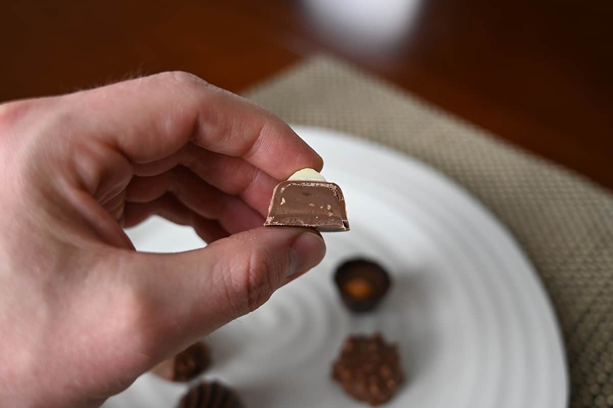 Image of a hand holding one sweet almond chocolate close to the camera cut in half so you can see the center.