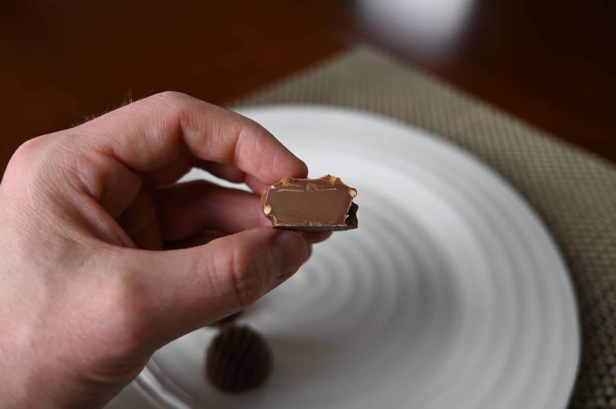 Image of a hand holding one hazelnut cluster chocolate close to the camera cut in half so you can see the center.