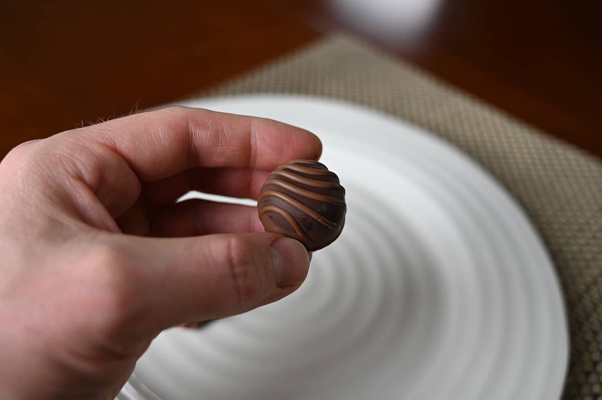 Image of a hand holding one caramel cluster chocolate close to the camera with a plate of chocolates in the background.