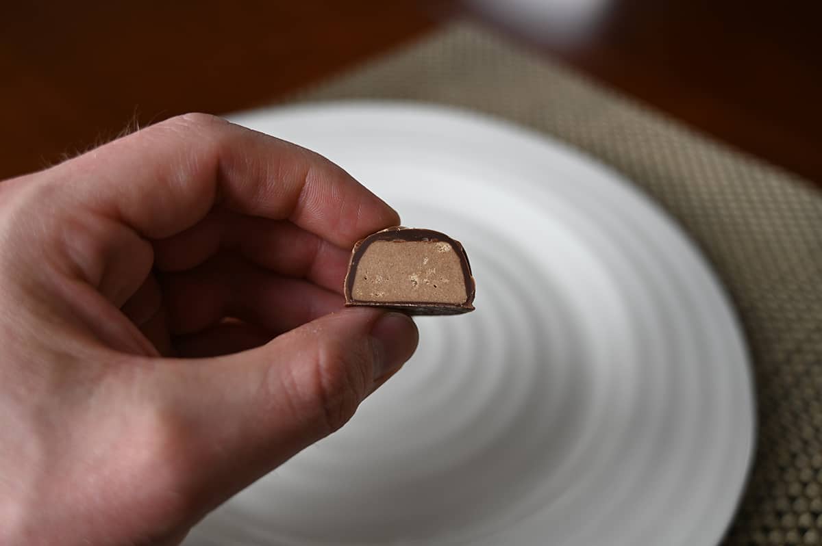 Image of a hand holding one caramel cluster chocolate close to the camera cut in half so you can see the center.