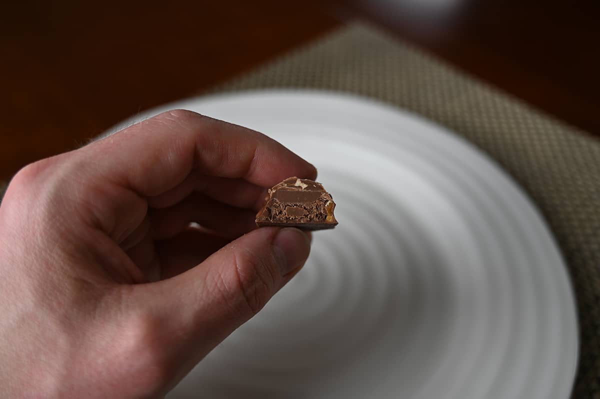 Image of a hand holding one crunchy praline chocolate close to the camera cut in half so you can see the center.