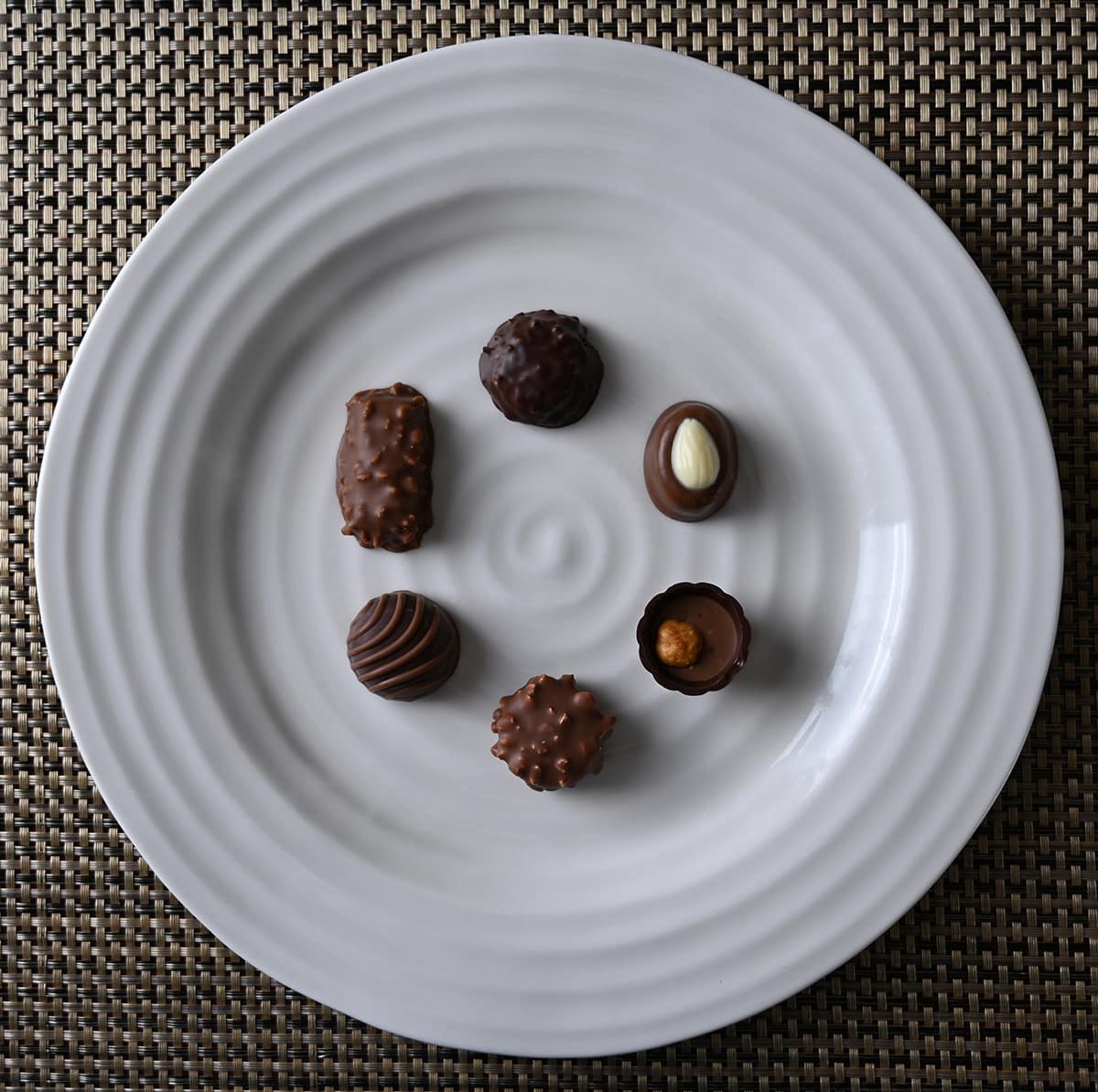 Top down image of a plate with six different kinds of chocolates on it in a circular shape.