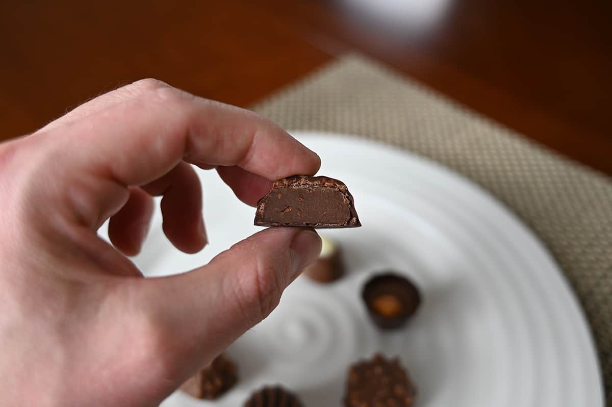 Image of a hand holding one dark cluster chocolate close to the camera cut in half so you can see the center.