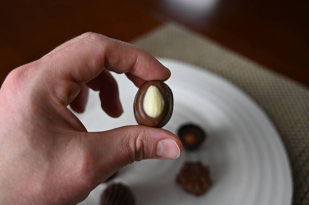 Image of a hand holding one sweet almond chocolate close to the camera with a plate of chocolates in the background.