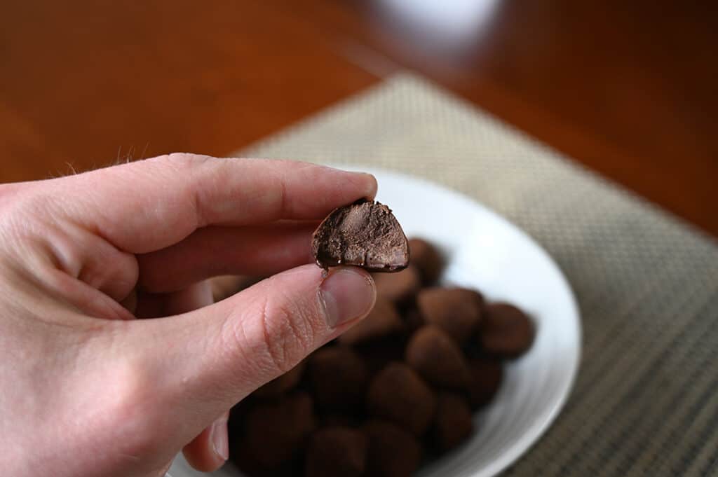 Closeup side view image of a hand holding a truffle with a bite taken out of it with truffles in a bowl in the background.