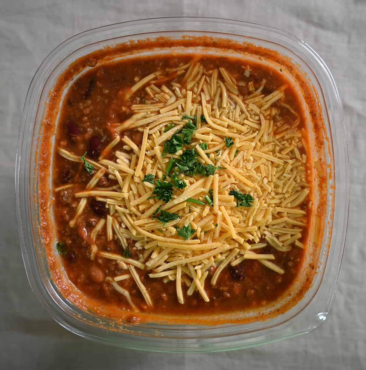 Top down image of an open container of Kirkland Signature Beef Chili showing cheese and parsley on top.