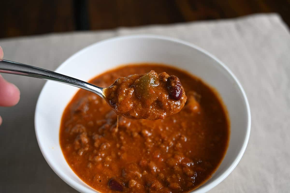 Top down image of a bowl of chili with a spoon scooping some out of the bowl. On the spoon is green pepper, kidney beans and tomatoes.
