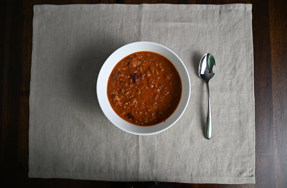 Top down image of a bowl of chili served in a white bowl beside a spoon.