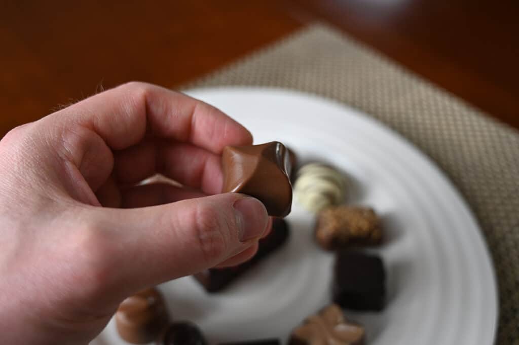 Image of a hand holding a lina chocolate close to the camera. 