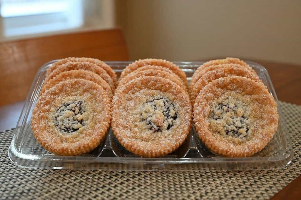 Side image of the Costco Kirkland Signature Raspberry Crumble Cookies in their plastic container  with the lid off, showing the cookies and what they look like, sitting on a table 