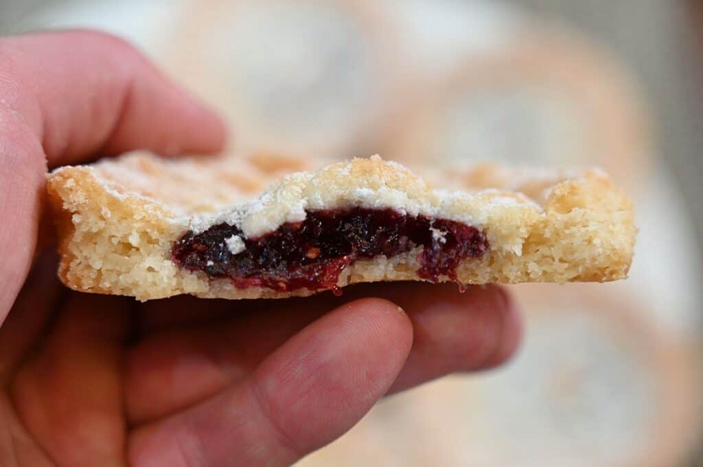 Close up image of a Costco Kirkland Signature Raspberry Crumble Cookie with a few bites taken out of it so you can see the raspberry inside