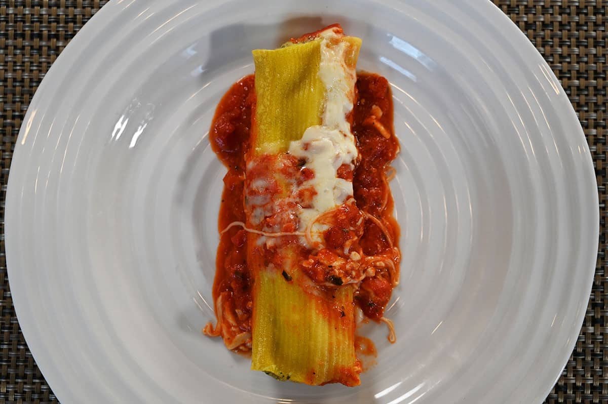 Top down image of one piece of Four Cheese and Spinach Manicotti cooked and served on a white plate. 