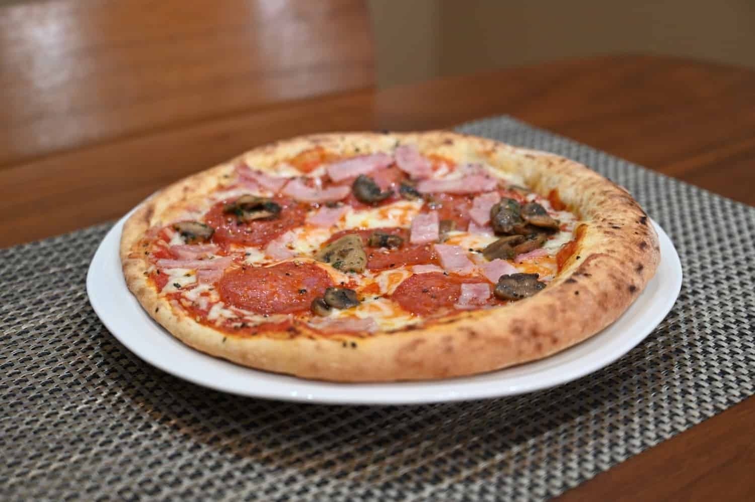 Sideview image of the bacon, mushroom and salami pizza cooked and served on a white plate.