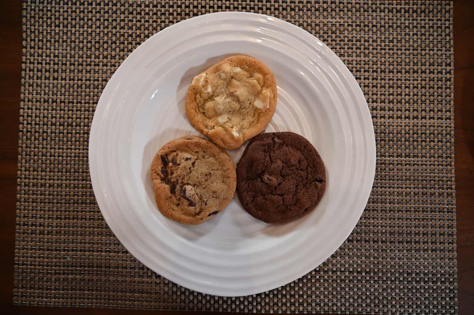 A white chocolate macadamia nut cookie, a triple chocolate cookie and a chocolate chunk cookie on a plate photographed from above.