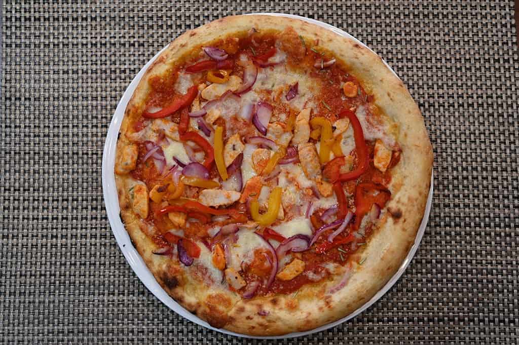 Top down image of a chicken and grilled peppers pizza cooked and served on a white plate.