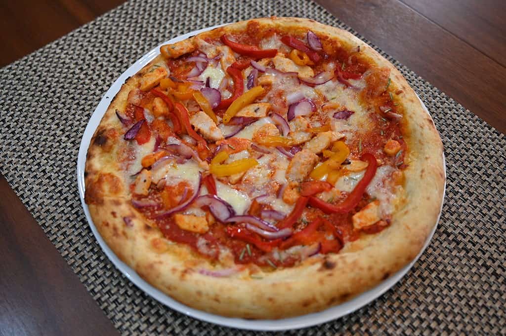 Side view top down image of a chicken and grilled peppers pizza cooked and served on a white plate.