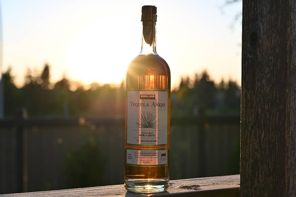 Image of the anejo tequila bottle outside on a deck unopened with the sun setting behind it.