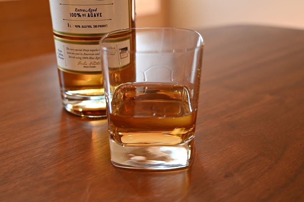 Image of the anejo tequila poured into a glass sitting on an oak table.