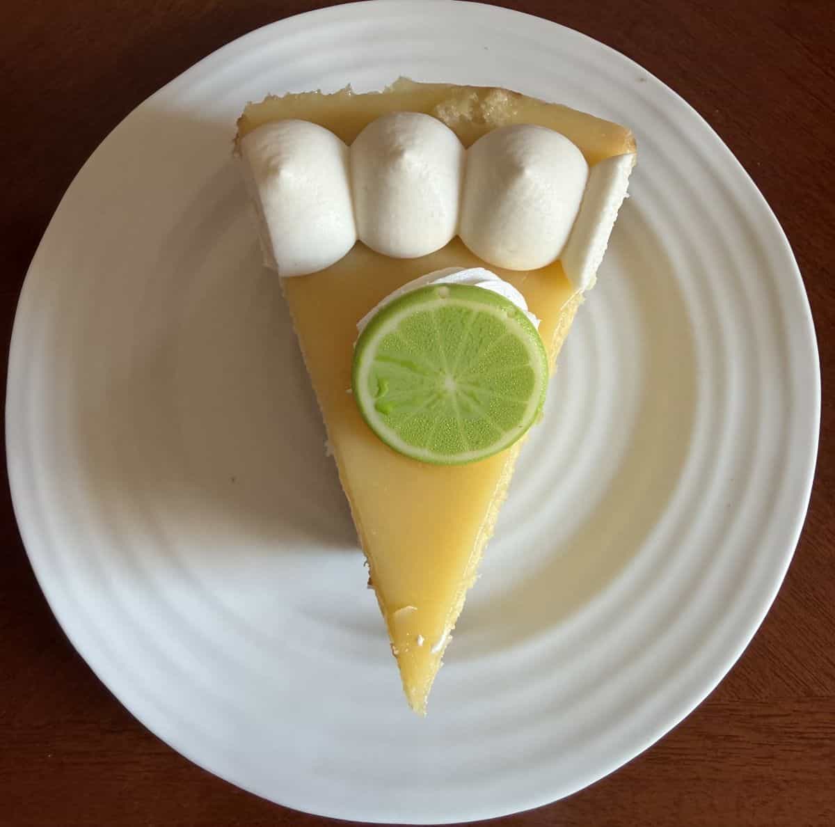 Top down image of one slice of key lime cake on a white plate with a white chocolate slice of lime on top.