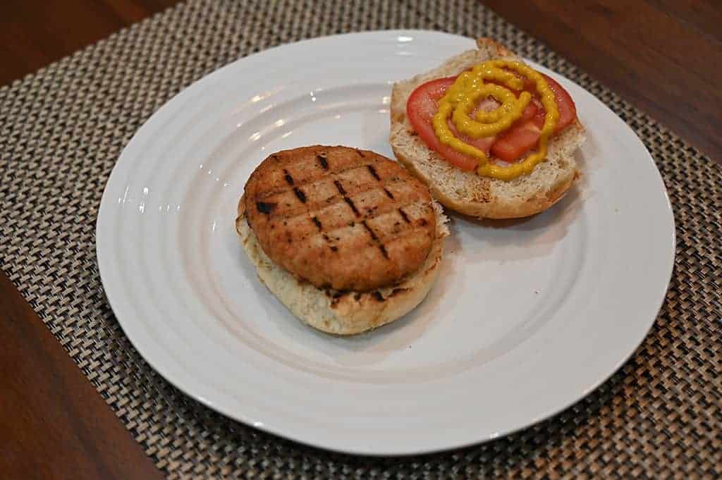 Image of a heated chicken burger patty on top of a bun with tomato and mustard.