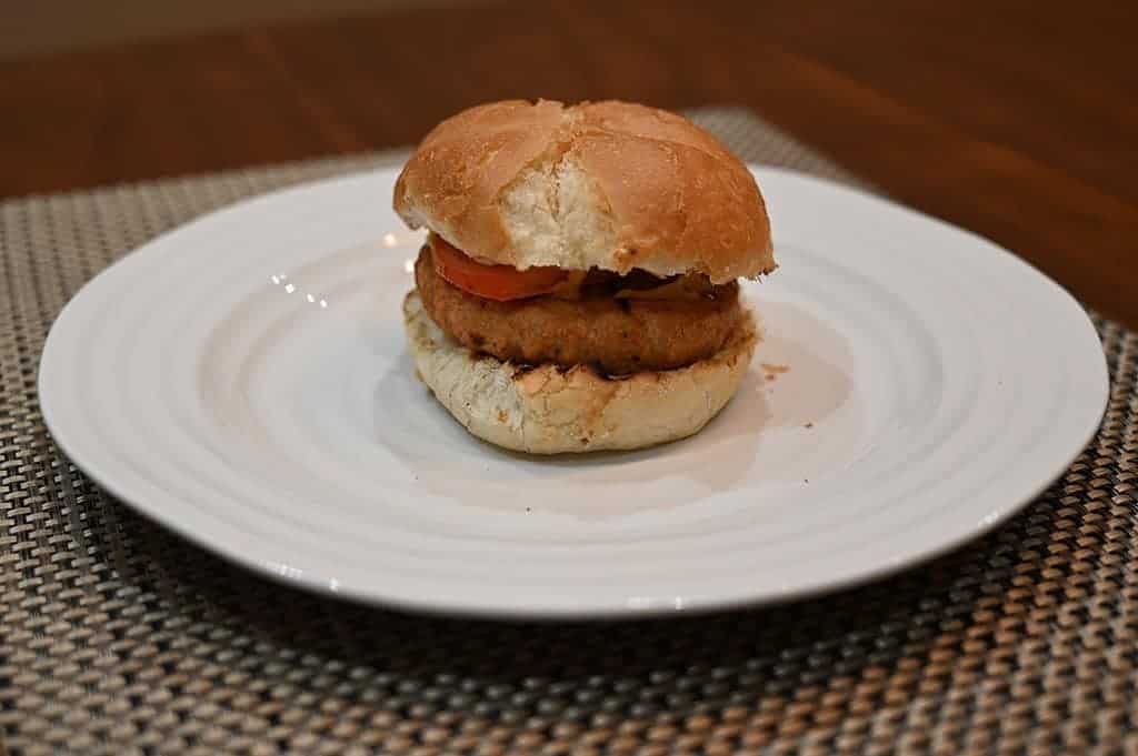 Image of a chicken burger in a bun with tomato served on a white plate. 