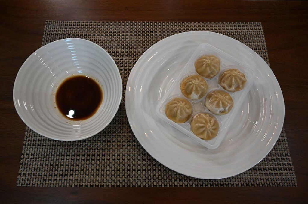 A tray of the Bibigo Steamed Dumplings along with a bowl of the sauce included in the box.