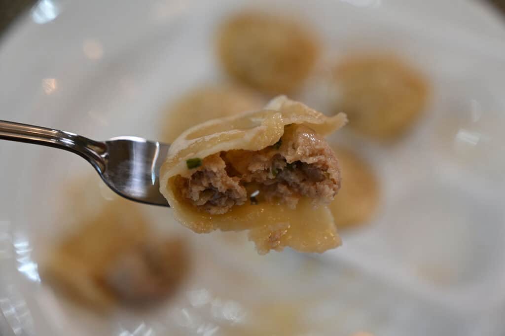 A close-up of a dumpling with a bite out of it, showing the filling inside.
