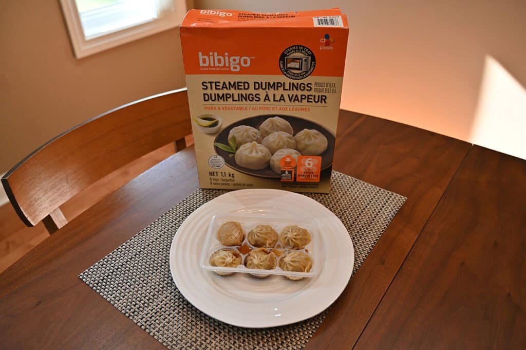 A tray of the dumplings sitting in front of the box with the sauce in the tray along with the dumplings.