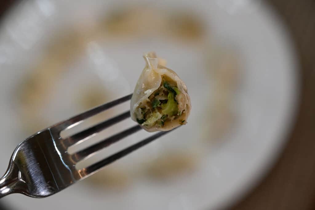 A close-up of a mini wonton on a fork with a bite taken out of it to show the filling inside.