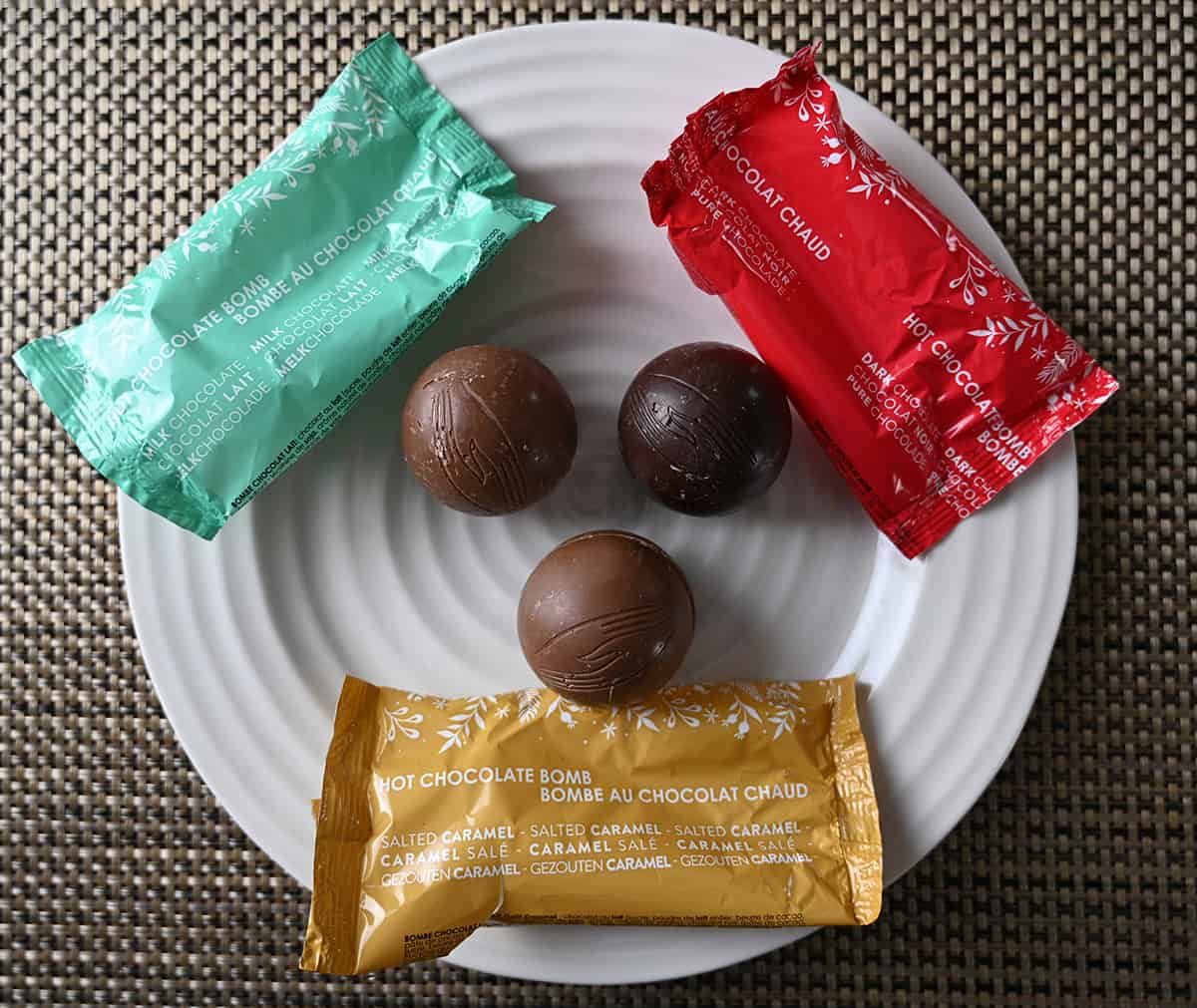 Image of three hot chocolate bombs unwrapped sitting on a plate, there is salted caramel, milk chocolate and dark chocolate.