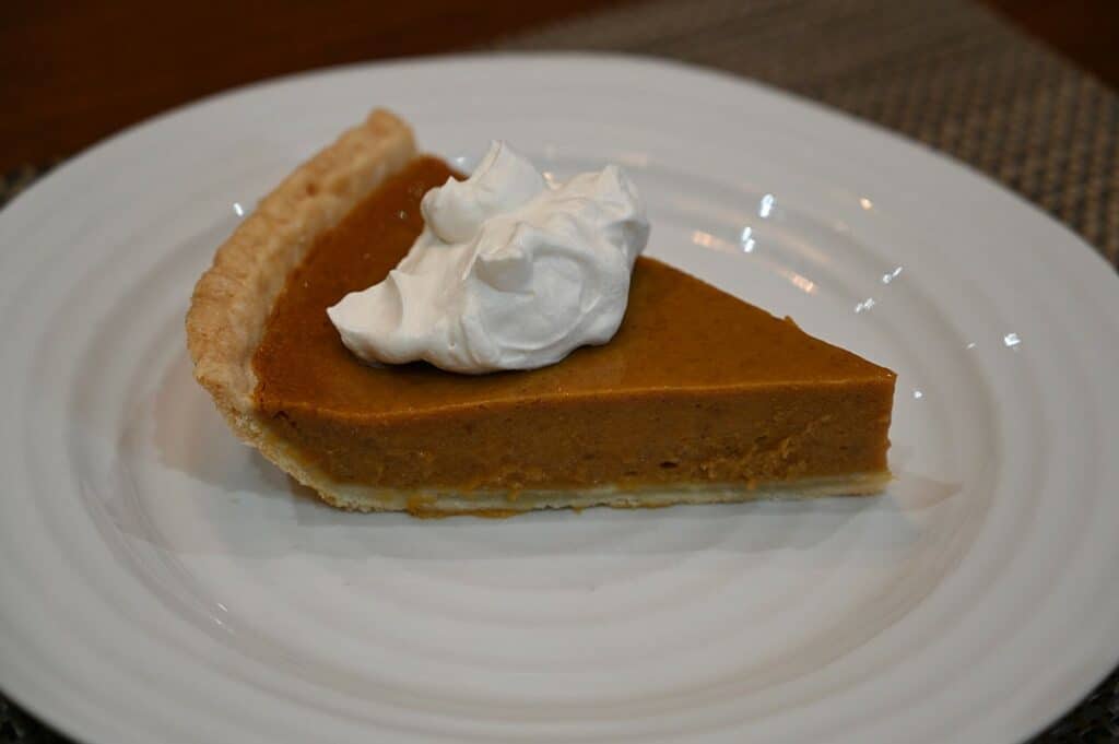 A slice of Kirkland Signature Pumpkin Pie with whipped cream on top on a plate.
