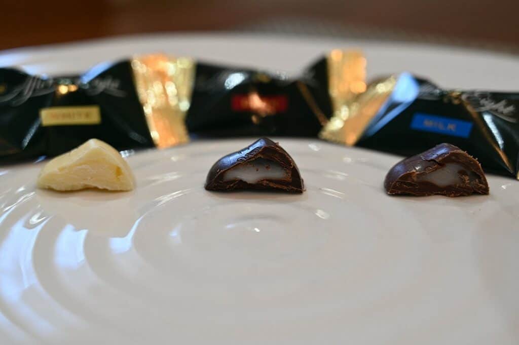 Image of the Costco After Eight Assorted Mint Pieces on a plate from left to right white chocolate, milk chocolate and dark chocolate with a bite taken out to show the filling