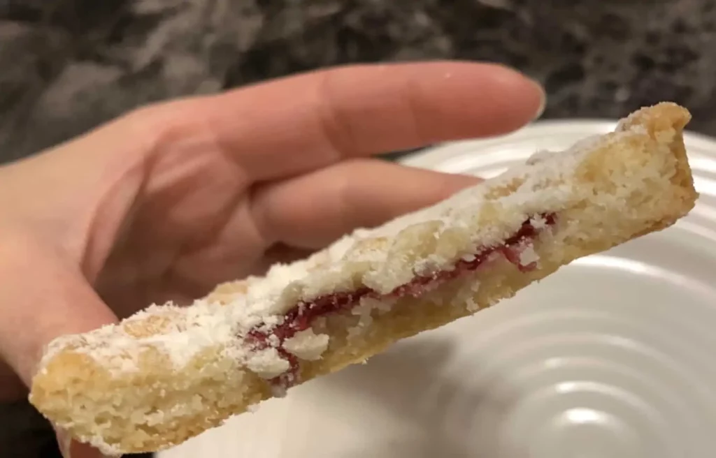 A close-up photo of a Kirkland Signature Raspberry Crumble Cookie with a bite out of it to show the raspberry filling inside.
