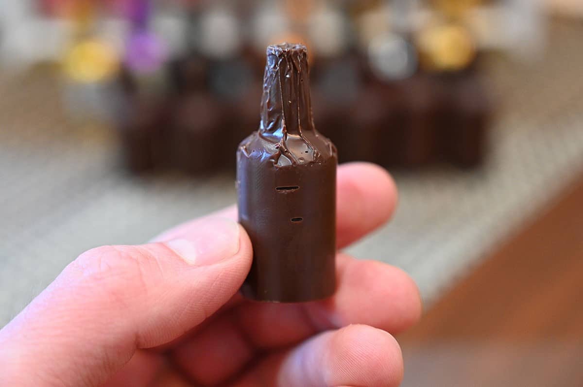 A close-up image of a hand holding an unwrapped chocolate.