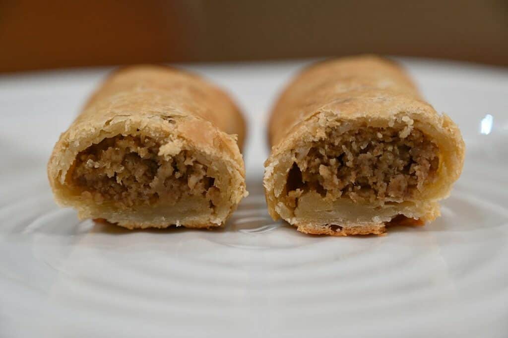 Closeup image of two Costco Prairie Creek Kitchen Sausage Beef Rolls cooked and cut open on a plate so you can see the inside