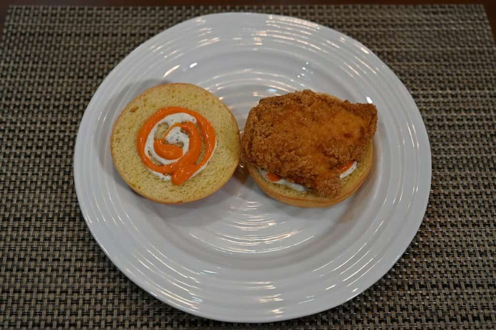 Image of the Costco Kirkland Signature Chicken Burger Meal Kit chicken burger cooked and plate with the bun open so you can see the sauce on the top of the bun 