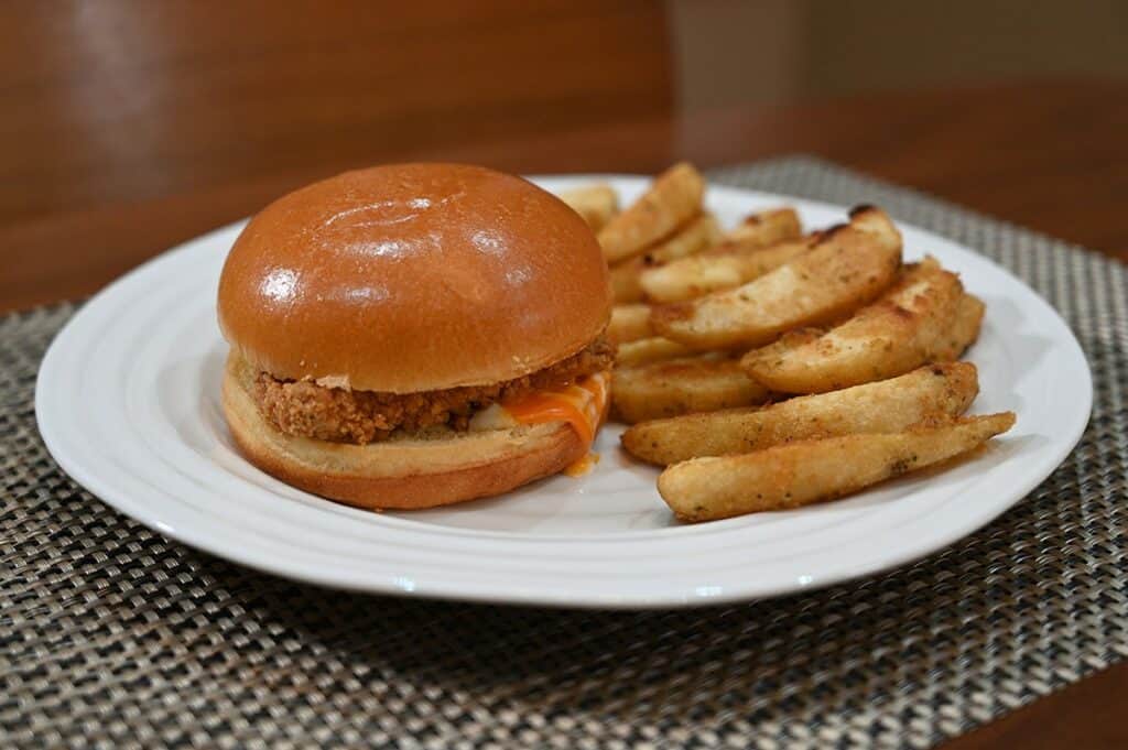 Image of the Costco Kirkland Signature Chicken Burger Meal Kit cooked and plated, one burger on the plate and a side of potato wedges, side view image