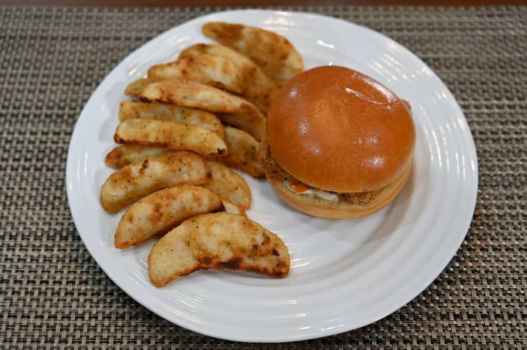 Image of the Costco Kirkland Signature Chicken Burger Meal Kit after cooking it, plated , one burger and potato wedges. Top down image. 