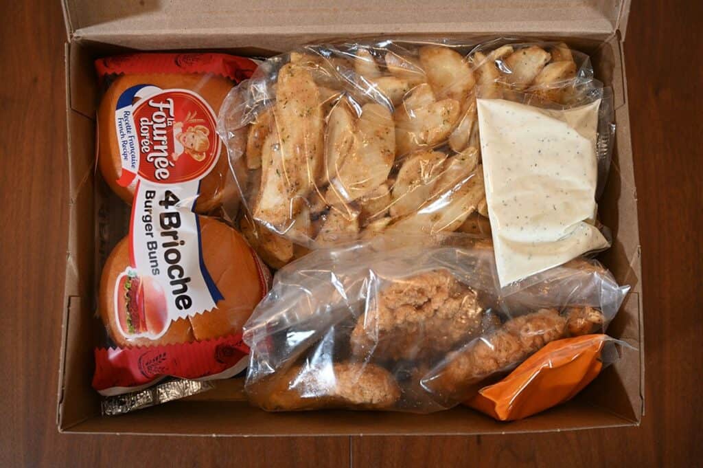 Image of the contents in the Costco Kirkland Signature Chicken Burger Meal Kit. BUns, chicken, potato wedges and two sauces. 