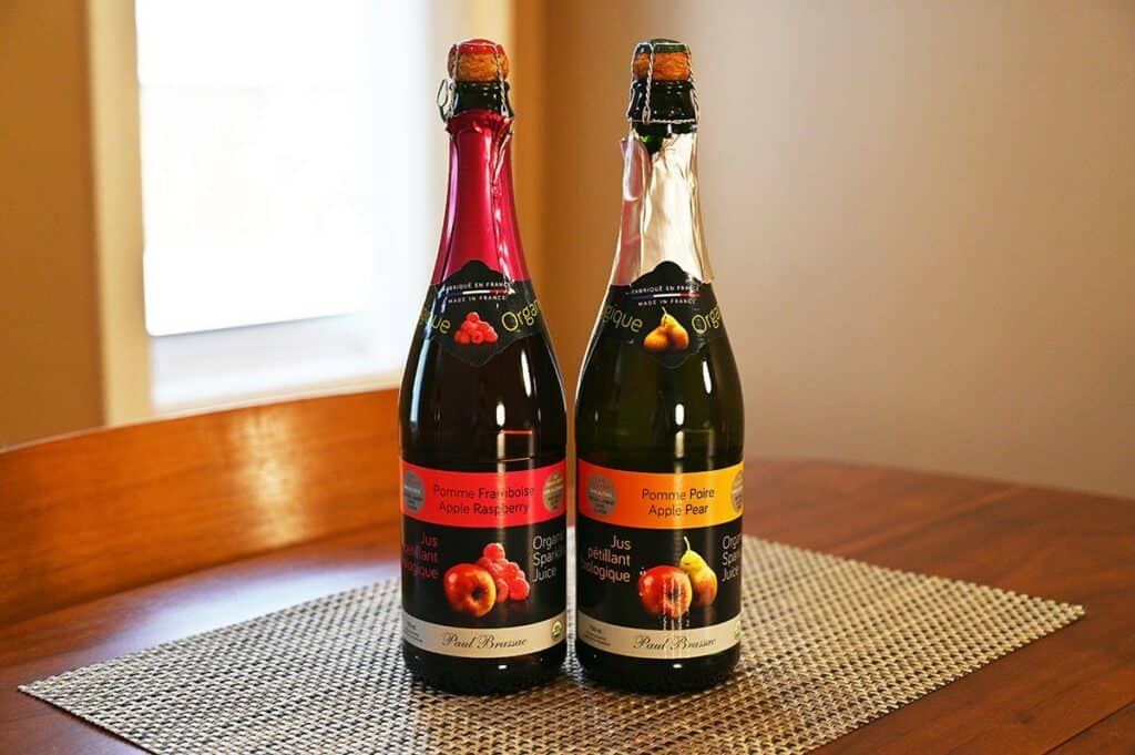 Sideview image of the Costco Paul Brassac Organic Sparkling Juice bottles unopened sitting on a table, left is apple raspberry right is apple pear. 
