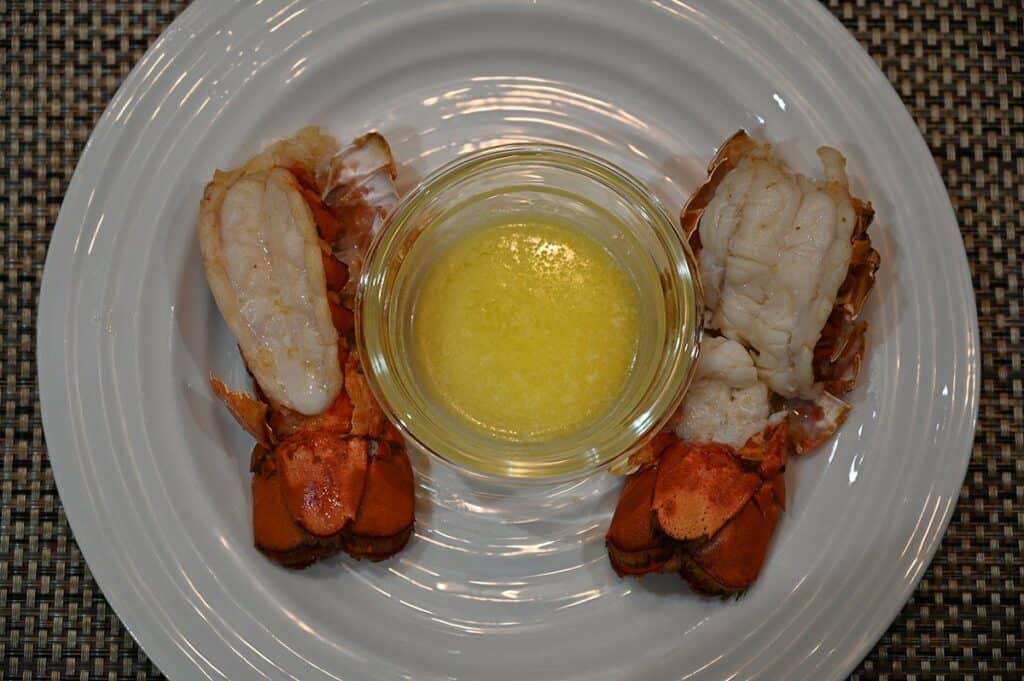 Top down image of two cooked Costco Seacore Frozen Lobster Tails with a side of garlic butter in the middle on the plate. 